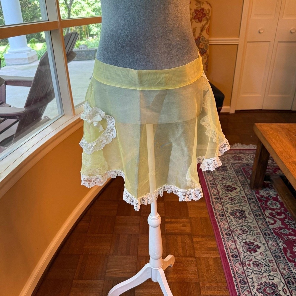 Vintage sheer yellow apron with ornate white lace trim and a bow-accented pocket